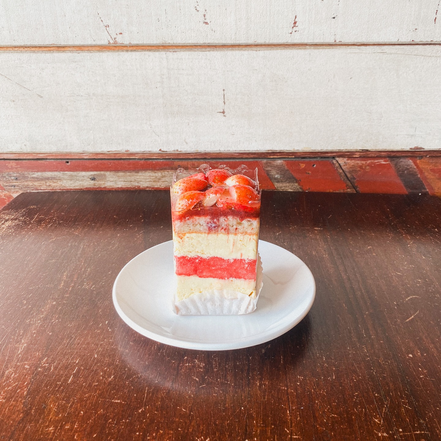 A slice of Rekindle's layered strawberry cream cake, topped with fresh strawberries, on a white plate