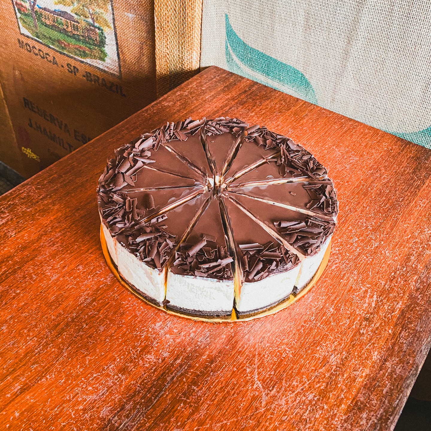 A whole chocolate cake finished with dark chocolate curls, resting on a timber table